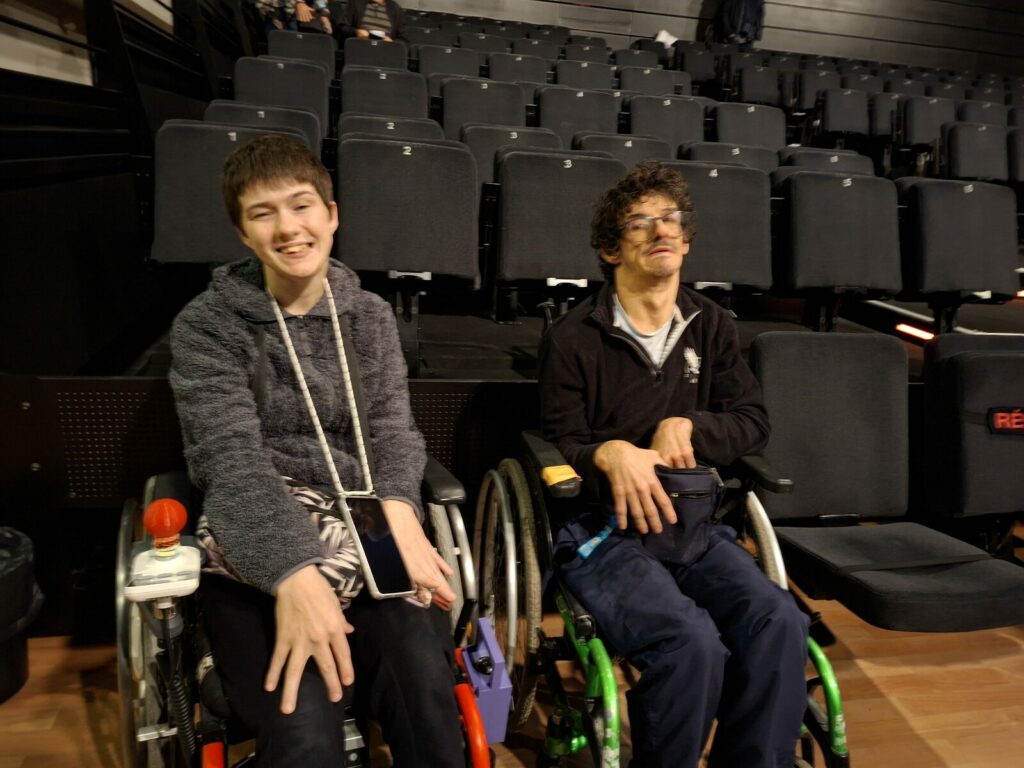 Amélie et Erwann, en fauteuil roulant, devant les gradins de la salle avant le début du spectacle.